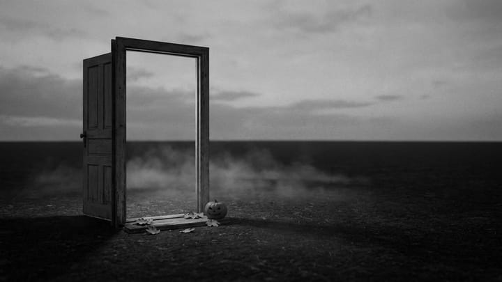 black-and-white photograph of a lone open doorway standing in an empty misty field, with fallen leaves and a small carved pumpkin on the threshold.